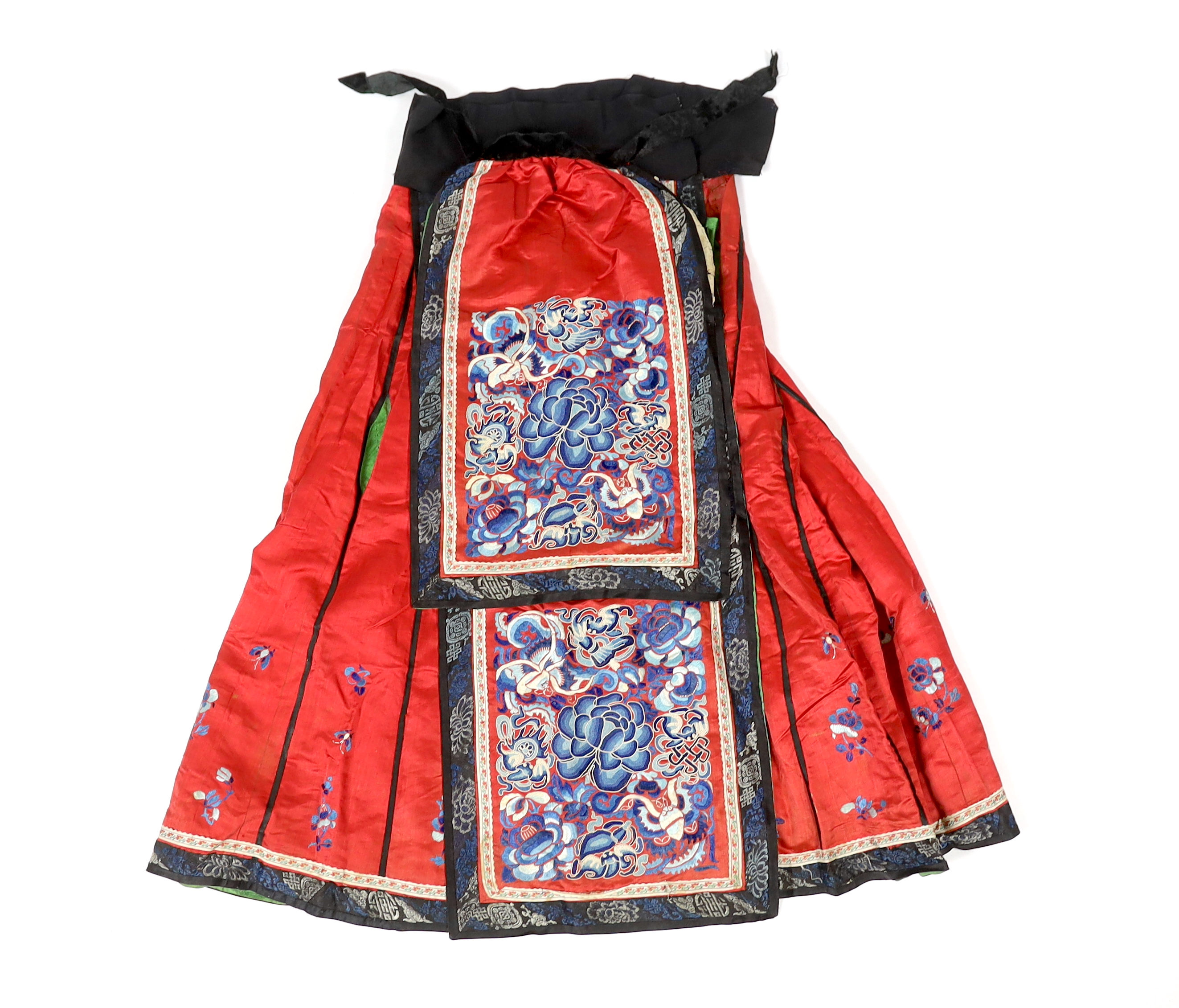 A Chinese red silk skirt, embroidered with a blue silk panel of Chinese knotting flowers and auspicious symbols, the bottom of the skirt with spot motifs bordered with embroidered braiding and ribbon, the slant is lined